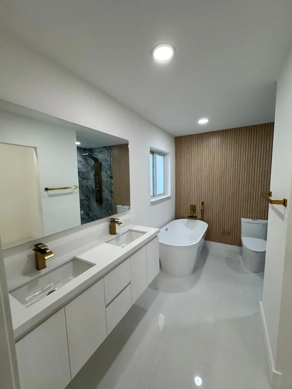 Double vanity with brass faucets, freestanding tub and oak slat accent wall