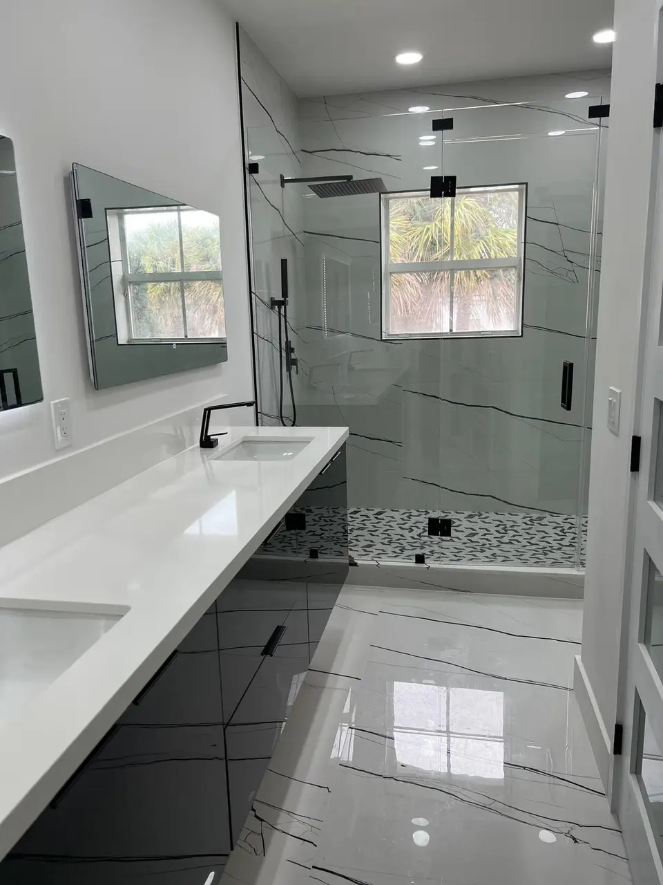 White double vanity with black faucets and glass shower with patterned floor