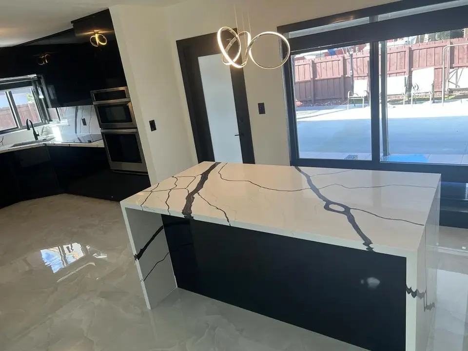 Marble-look waterfall island with black cabinetry and pendant lighting