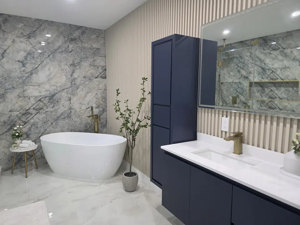 Bathroom with freestanding tub, navy tower cabinet, marble feature wall and brass faucet