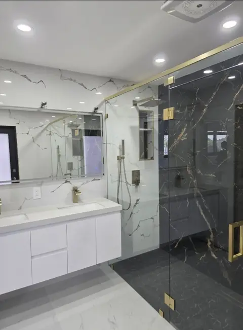 White marble vanity beside a dark marble shower with brass fixtures