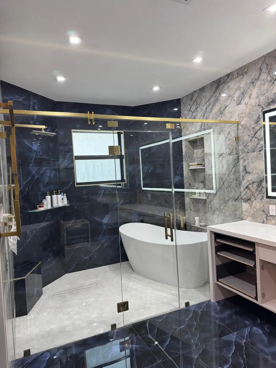 Shower in navy-blue marble-look porcelain with brass-framed glass and freestanding tub